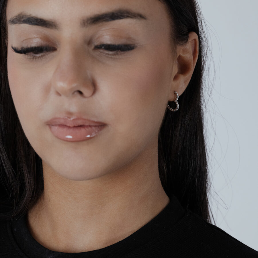 Aros de corazón plateados en una oreja, llevados por una persona con camiseta negra