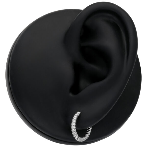 Pequeños pendientes de aro retorcidos en plata en un modelo de oreja negra sobre fondo blanco