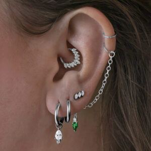 Varios pendientes en la oreja, incluyendo Little Tear Hoops negros con cristal verde.