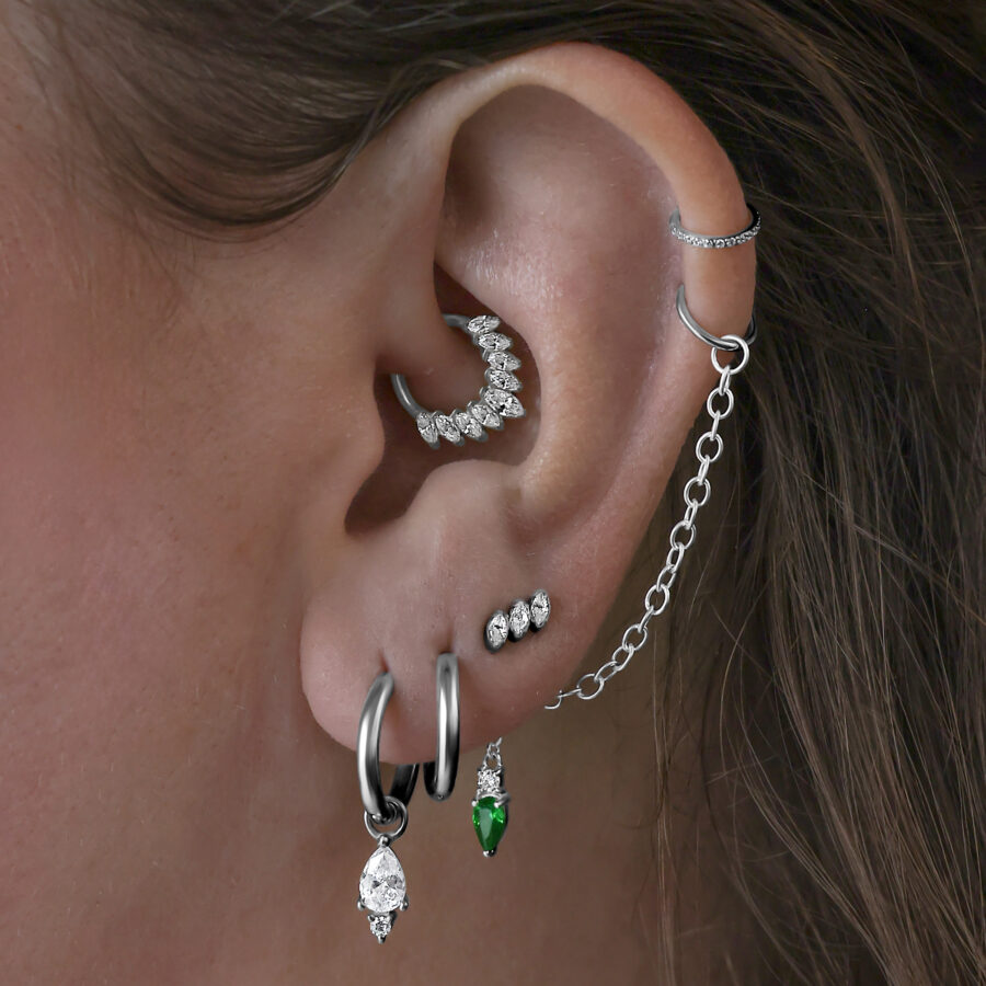 Varios pendientes en la oreja, incluyendo Little Tear Hoops negros con cristal verde.