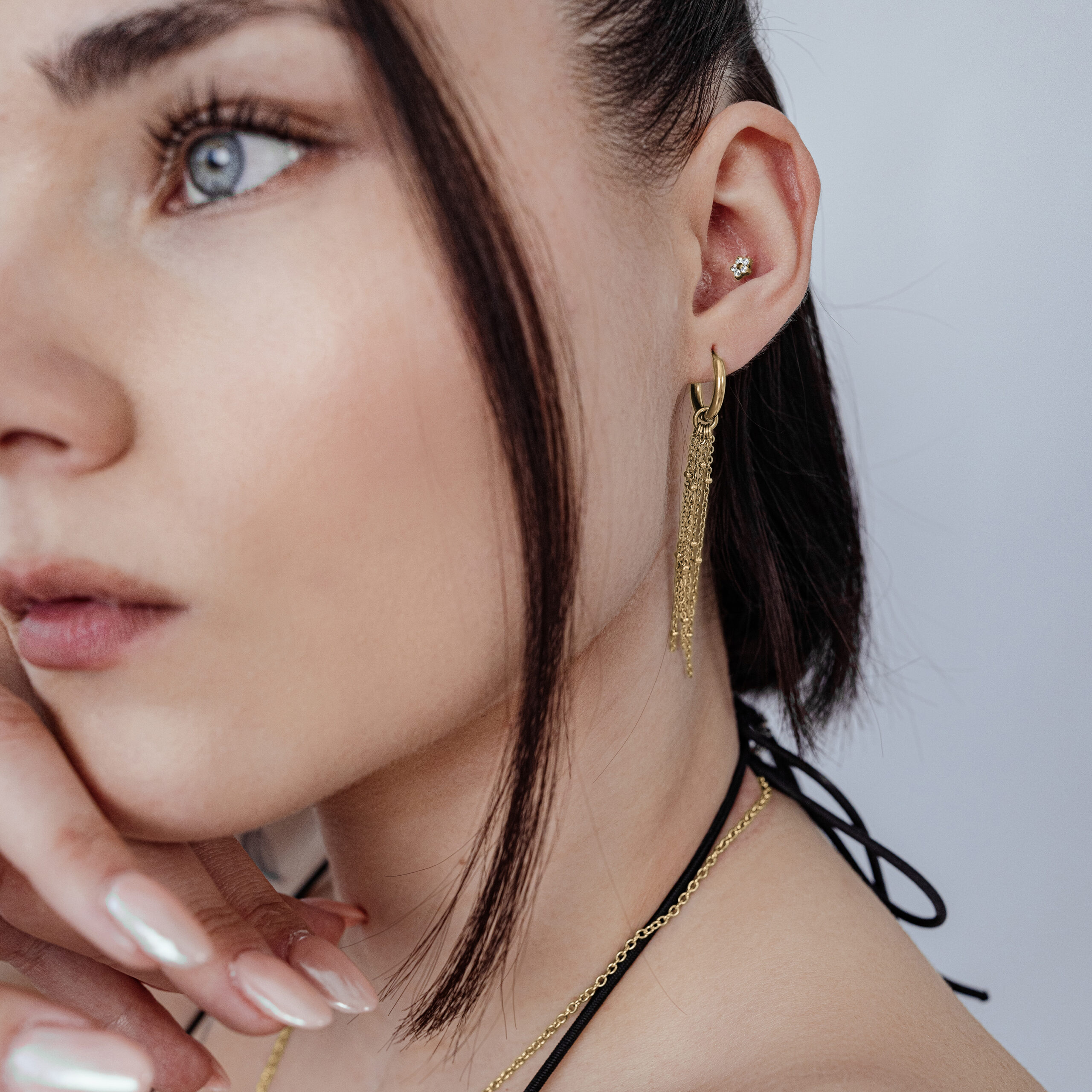 Primer plano de un adorno floral dorado con cristales en la oreja de una persona, fondo neutro