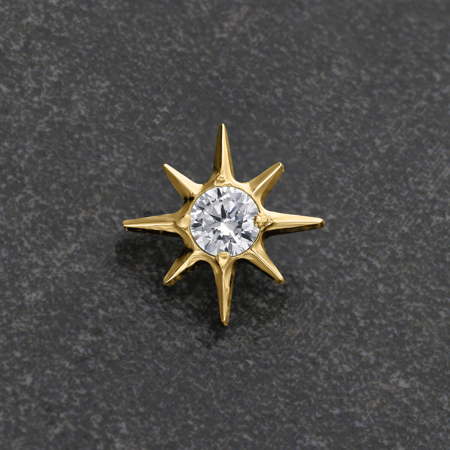 Ajuste metálico dorado en forma de estrella con cristal claro sobre fondo gris
