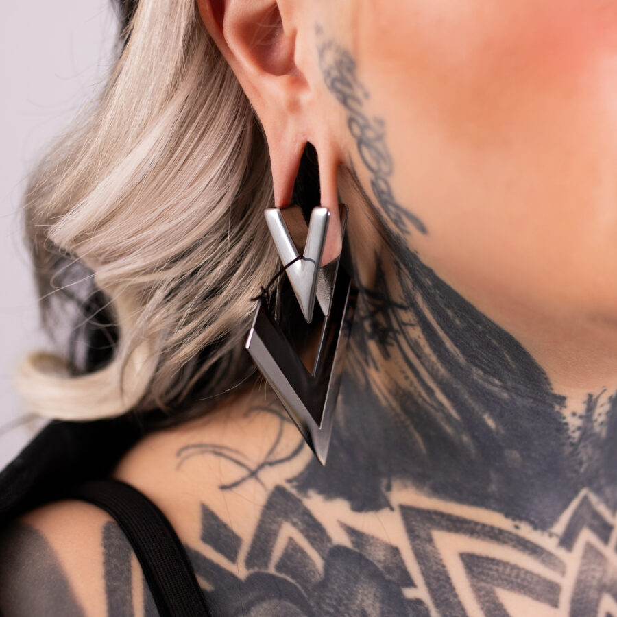 Aros en forma de V plateados y negros de acero quirúrgico en una oreja con tatuajes