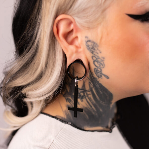 Aros cruzados negros de acero quirúrgico 316L en una oreja con tatuaje