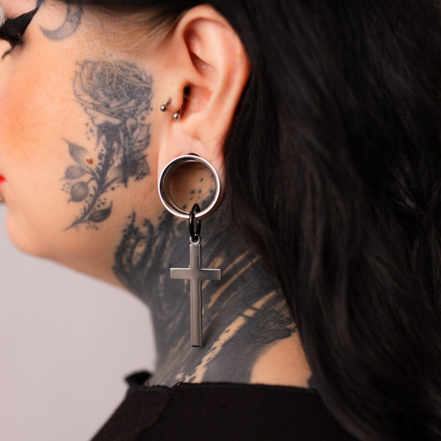 Pendientes cruzados plateados y negros en una oreja tatuada