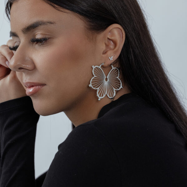 Aros de flores en plata en la oreja de una mujer con cabello oscuro, perfil lateral sobre fondo neutro