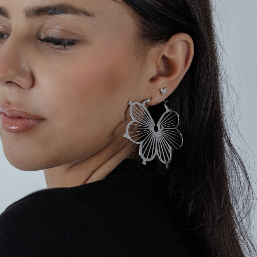 Pendientes de flores en plata en la oreja de una mujer con top negro, primer plano