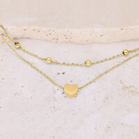 Pulsera de doble fila de metal dorado con colgante de corazón sobre fondo beige