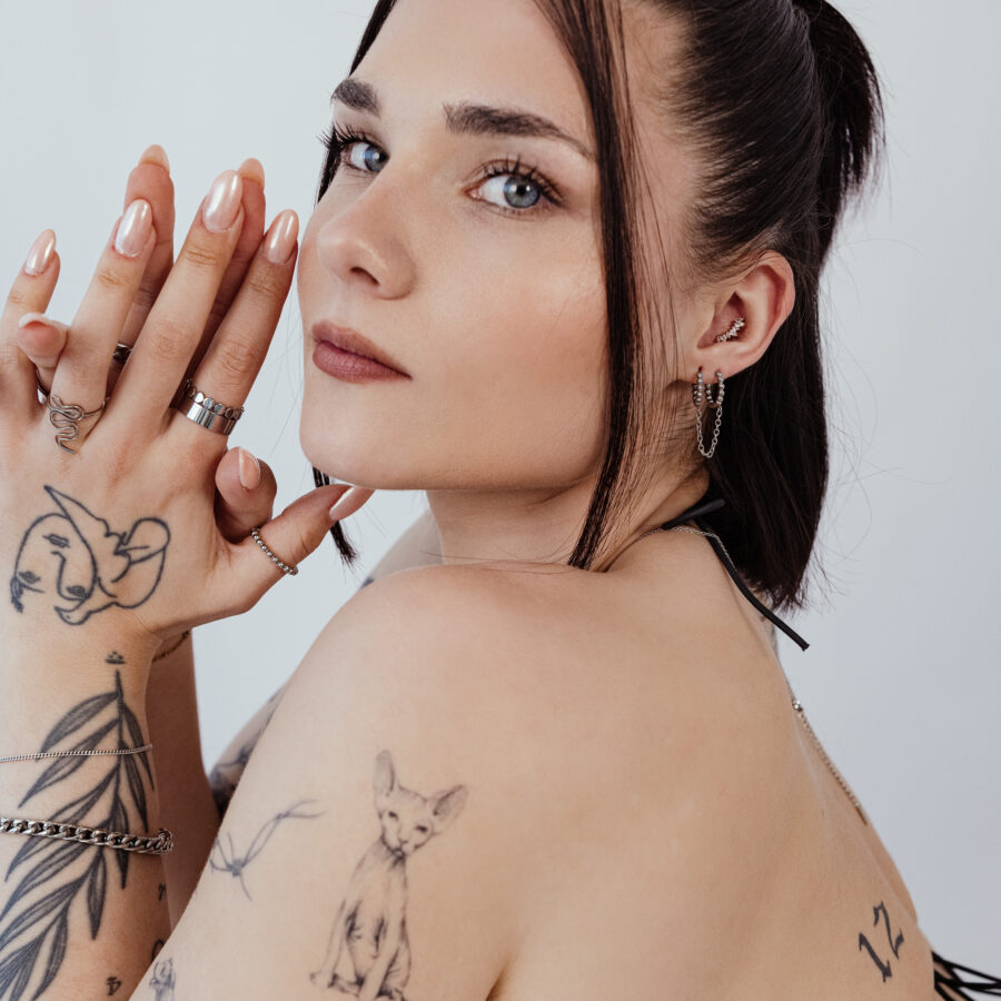 Mujer con brazos tatuados lleva aros de piercing negros y plateados en la oreja, perfil lateral