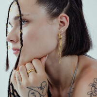 Mujer con pendientes triángulo dorado, de lado, cabello trenzado.