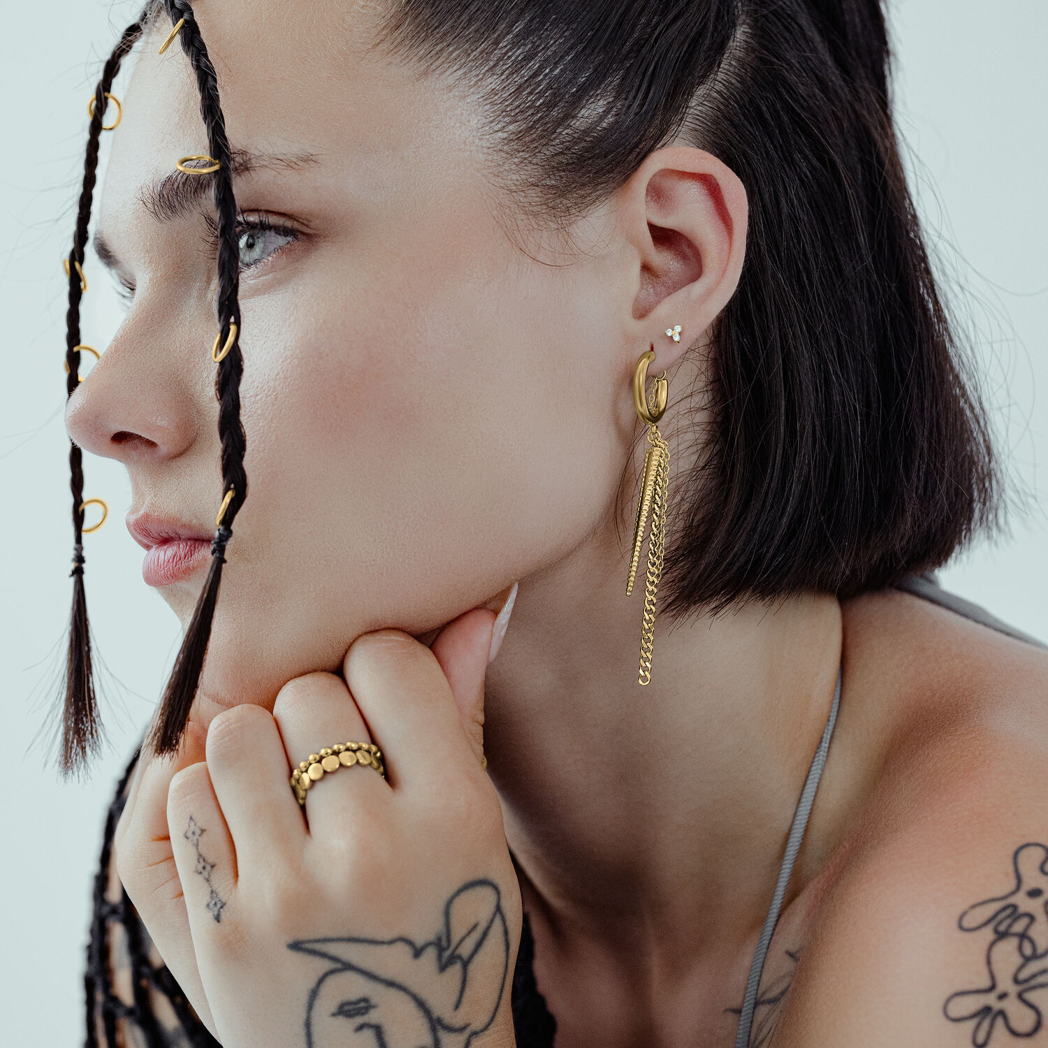 Mujer con pendientes triángulo dorado, de lado, cabello trenzado.