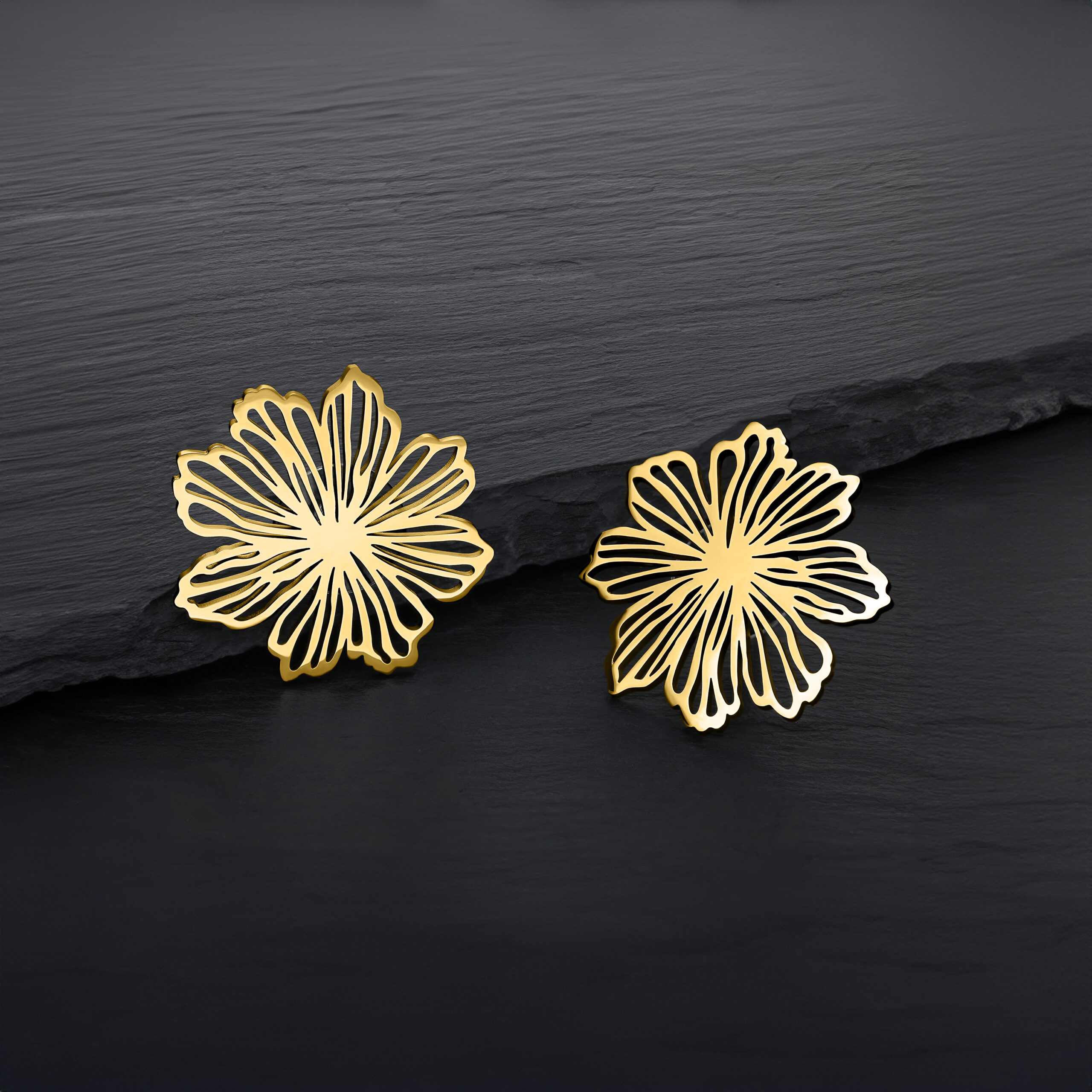 Pendientes de flores doradas de acero quirúrgico Dos pendientes de flores doradas sobre fondo oscuro