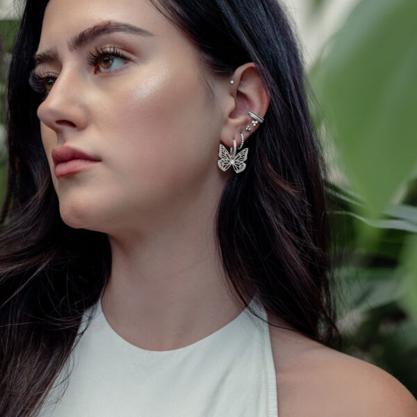 Mujer con pendientes de mariposa plateados, al aire libre, con plantas de fondo