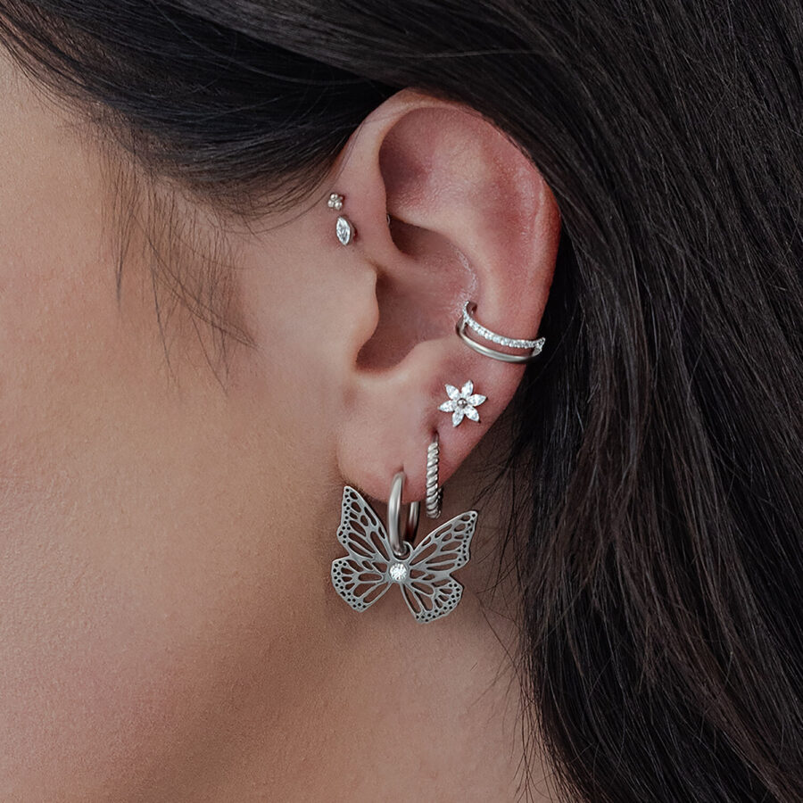 Pendientes Little Butterfly Hoops de plata en la oreja de una mujer, con otros pendientes