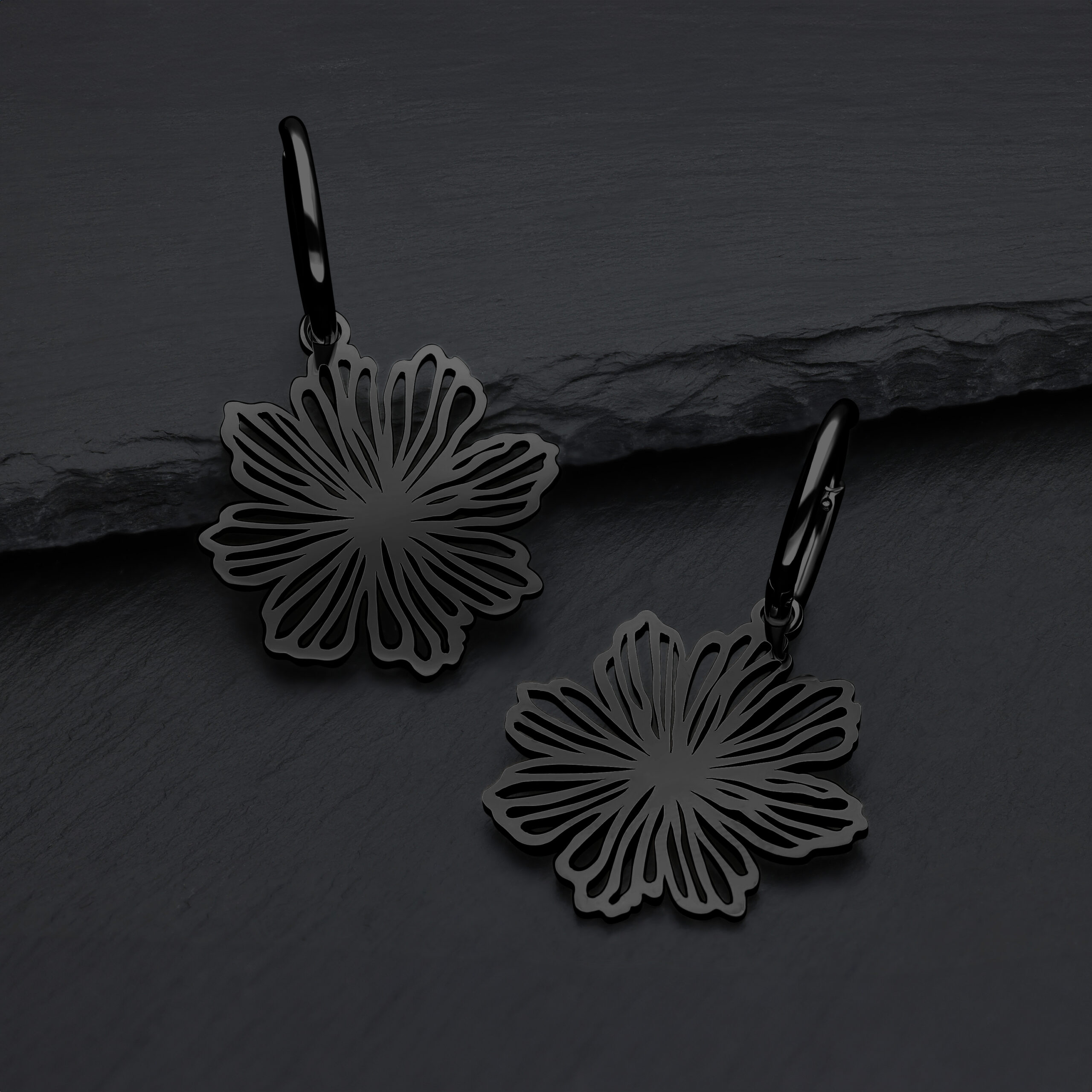 Pendientes negros en forma de flor de acero quirúrgico sobre fondo gris
