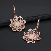 Zwei roségoldene Ohrringe mit Blumenmotiv auf dunklem Hintergrund
