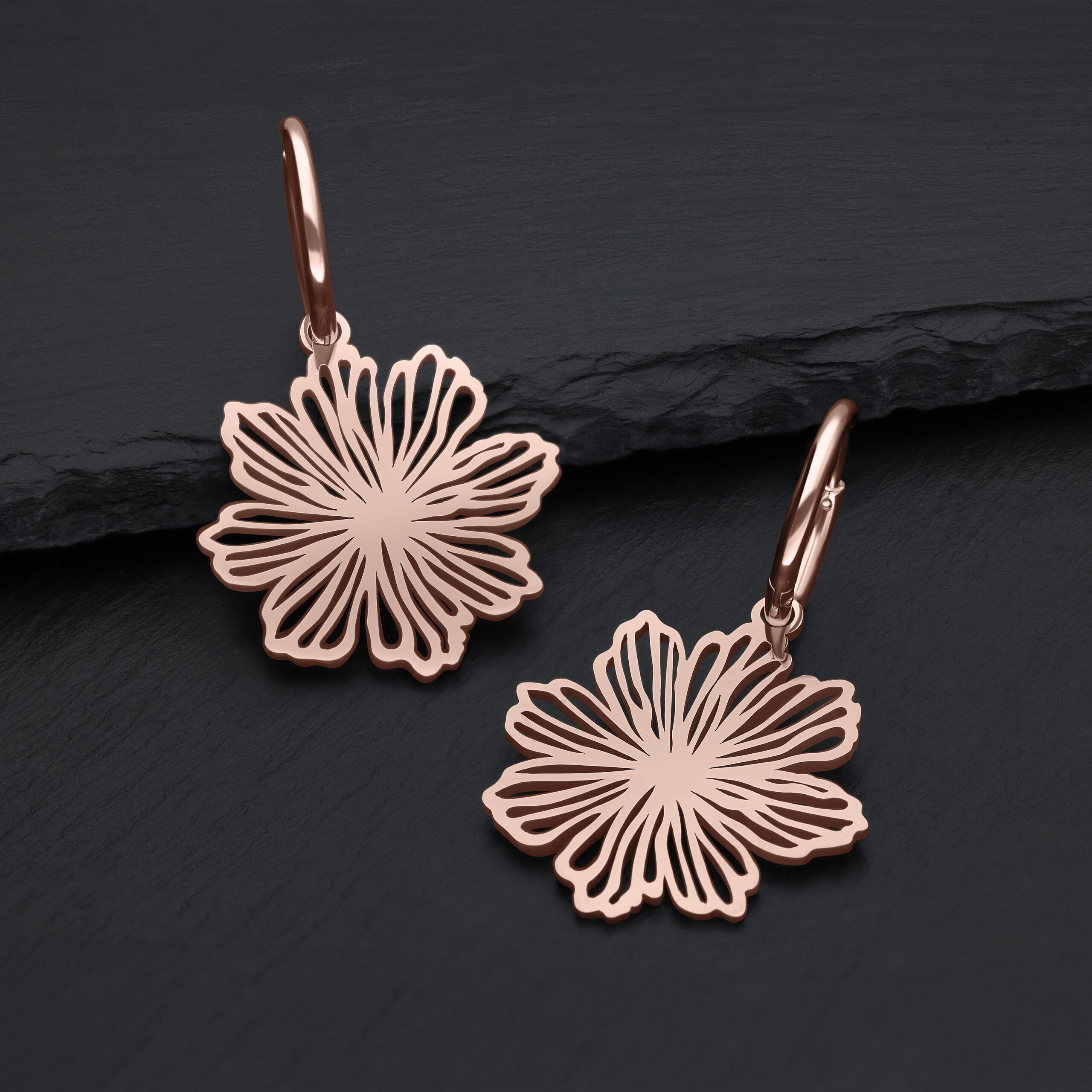 Zwei roségoldene Ohrringe mit Blumenmotiv auf dunklem Hintergrund