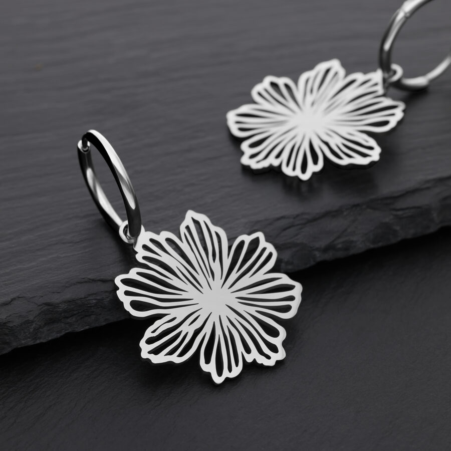Dos pendientes plateados con diseño de flores sobre fondo negro