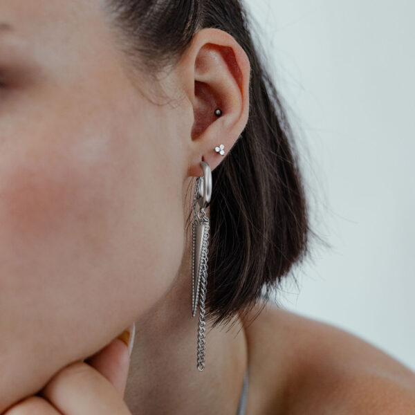 Pendientes de triángulo plateados en la oreja de una mujer con pelo corto frente a un fondo claro