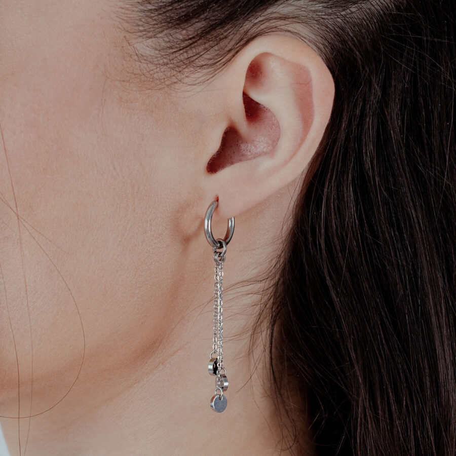 Aros plateados con colgante de cadena en oreja femenina sobre fondo claro