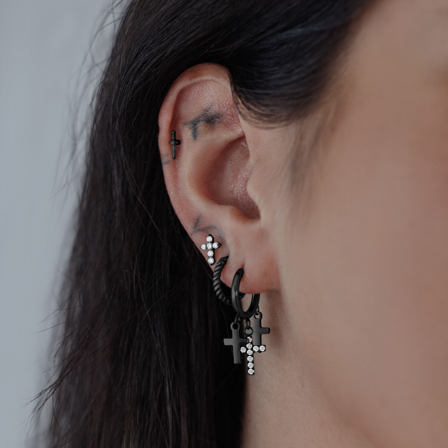 Schwarze Kreuz-Ohrringe aus Chirurgenstahl Schwarze Kreuz-Ohrringe an einem Ohr, glänzender Chirurgenstahl