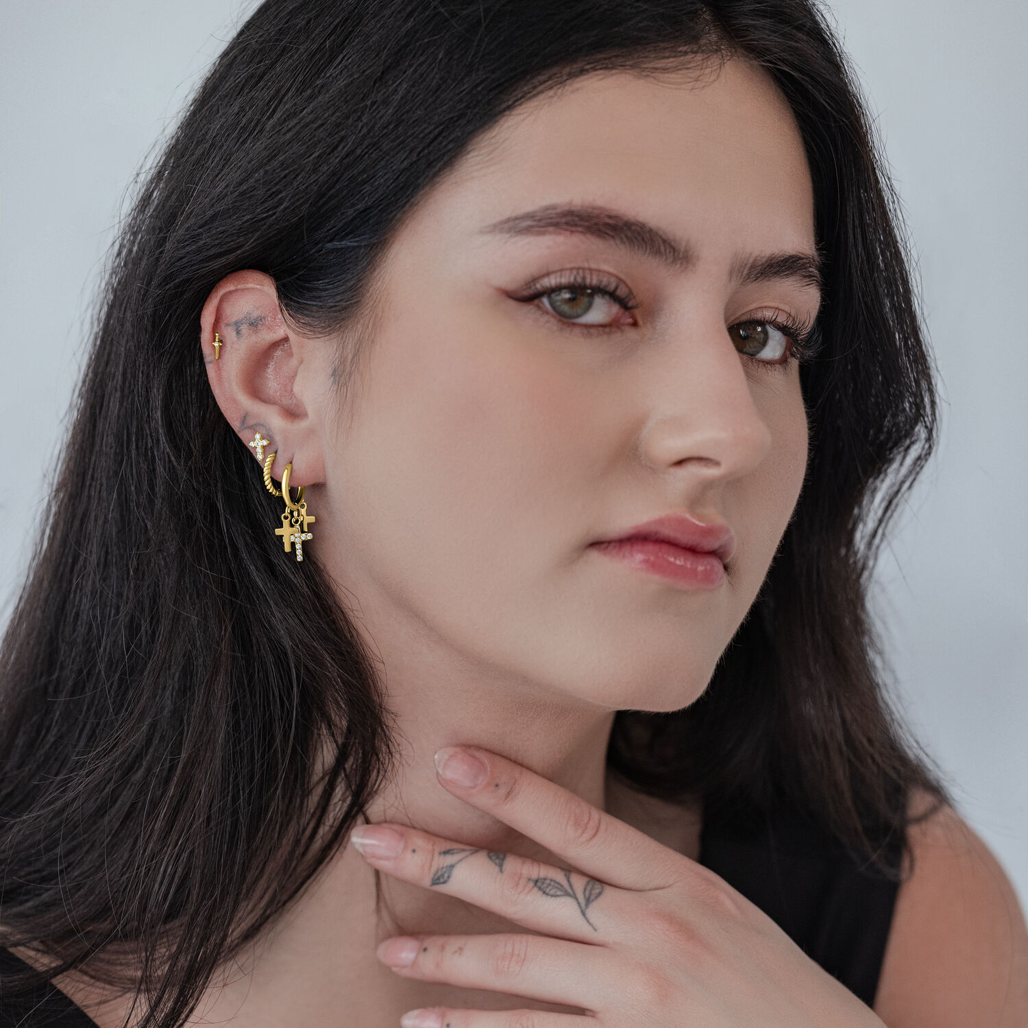 Mujer con aros de cruz dorados, brillantes, sobre fondo neutro