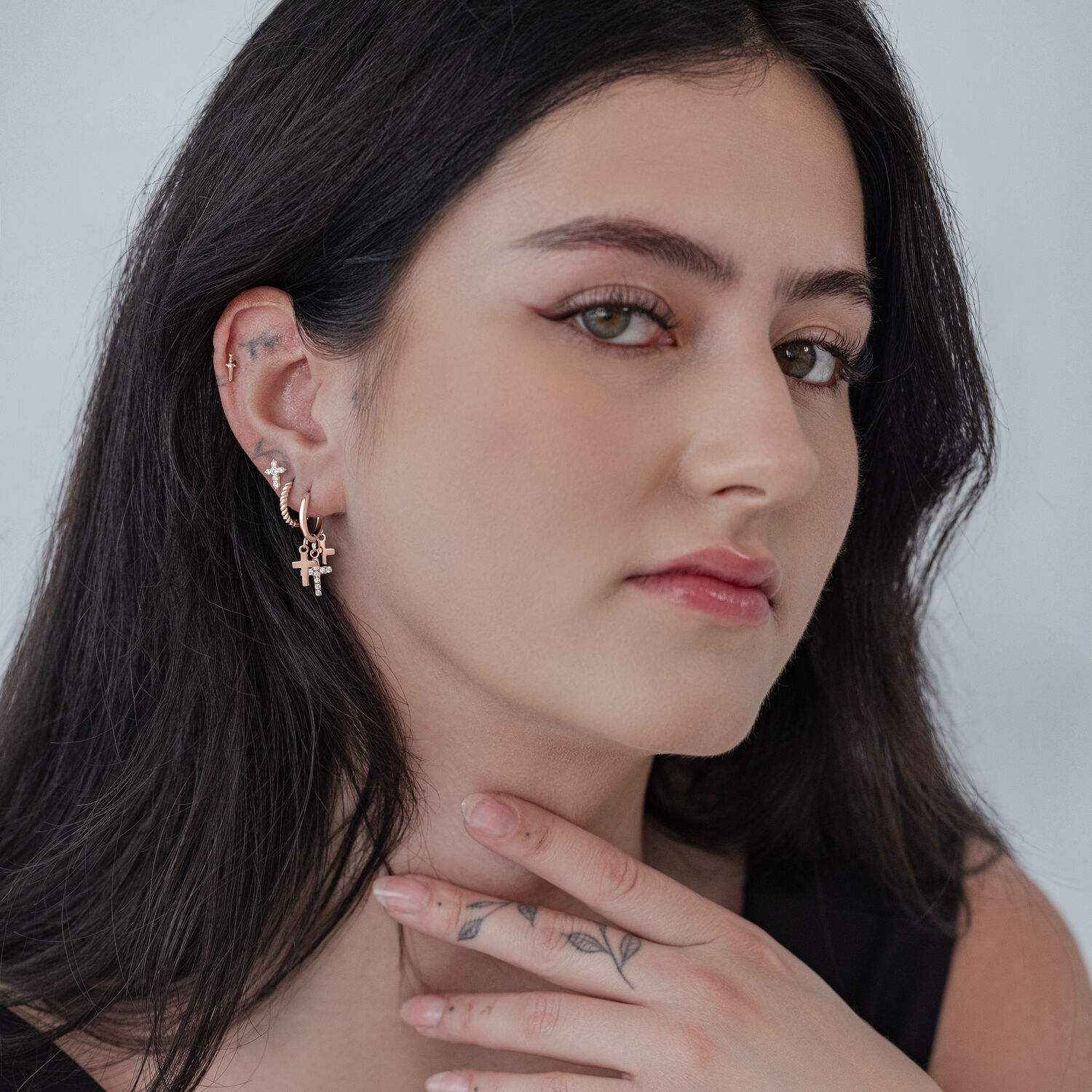Roségoldene Kreuz-Ohrringe am Ohr Frau mit roségoldenen kleinen Kreuz-Ohrringen vor neutralem Hintergrund
