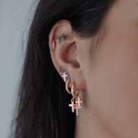 Roségold Creolen mit Kreuzanhänger Nahaufnahme von Creolen in Roségold mit kleinen Kreuzanhängern am Ohr.