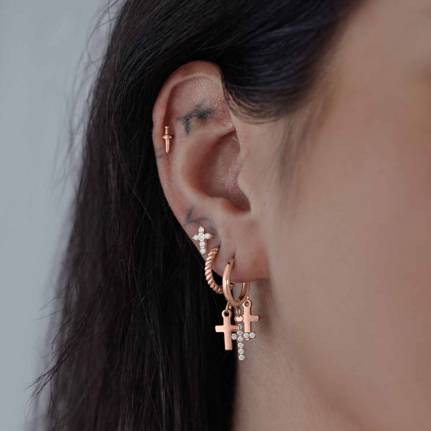 Roségold Creolen mit Kreuzanhänger Nahaufnahme von Creolen in Roségold mit kleinen Kreuzanhängern am Ohr.
