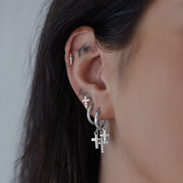 Aros de plata con colgantes de cruz en una oreja