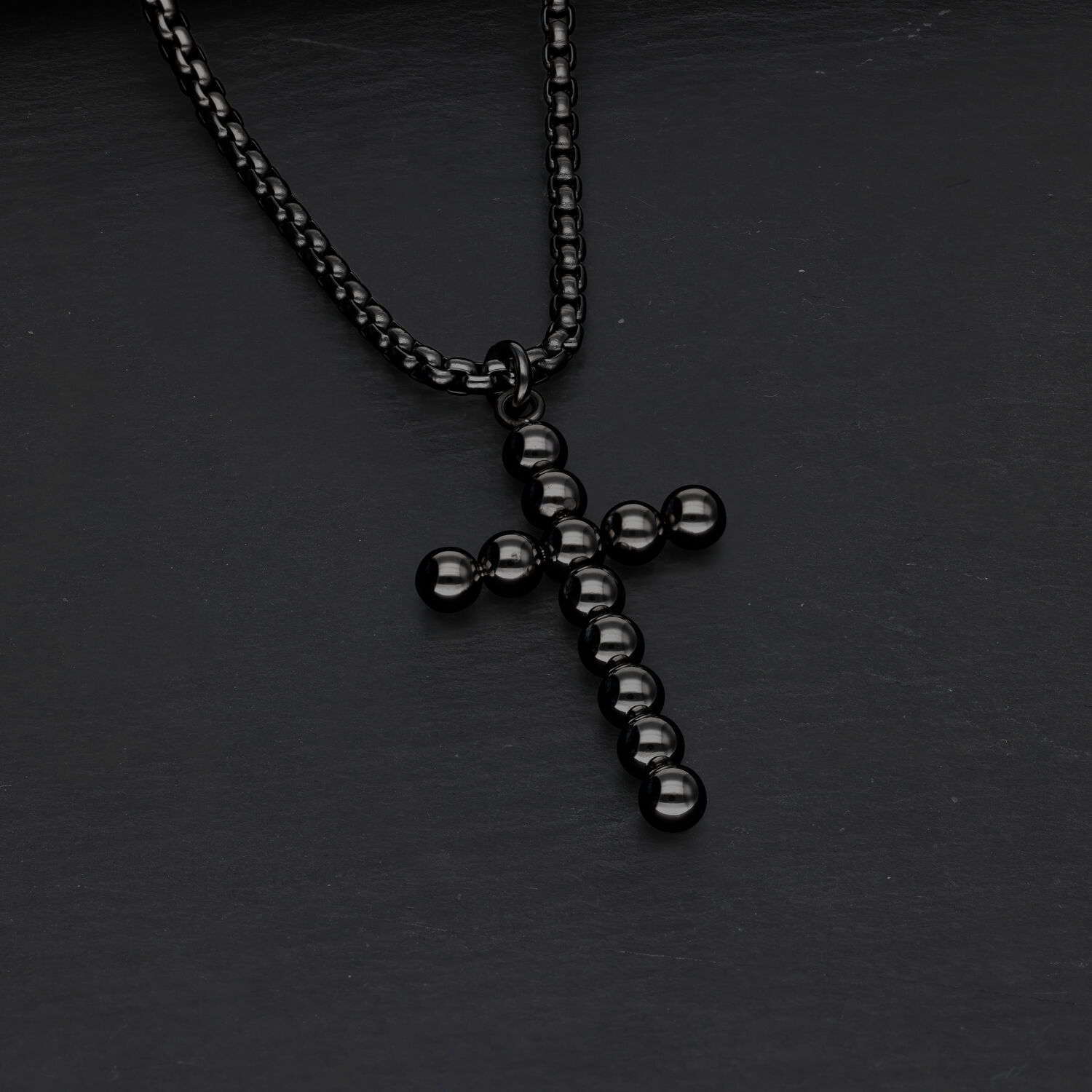 Schwarze Kreuzkette mit Kugeldesign auf dunklem Hintergrund