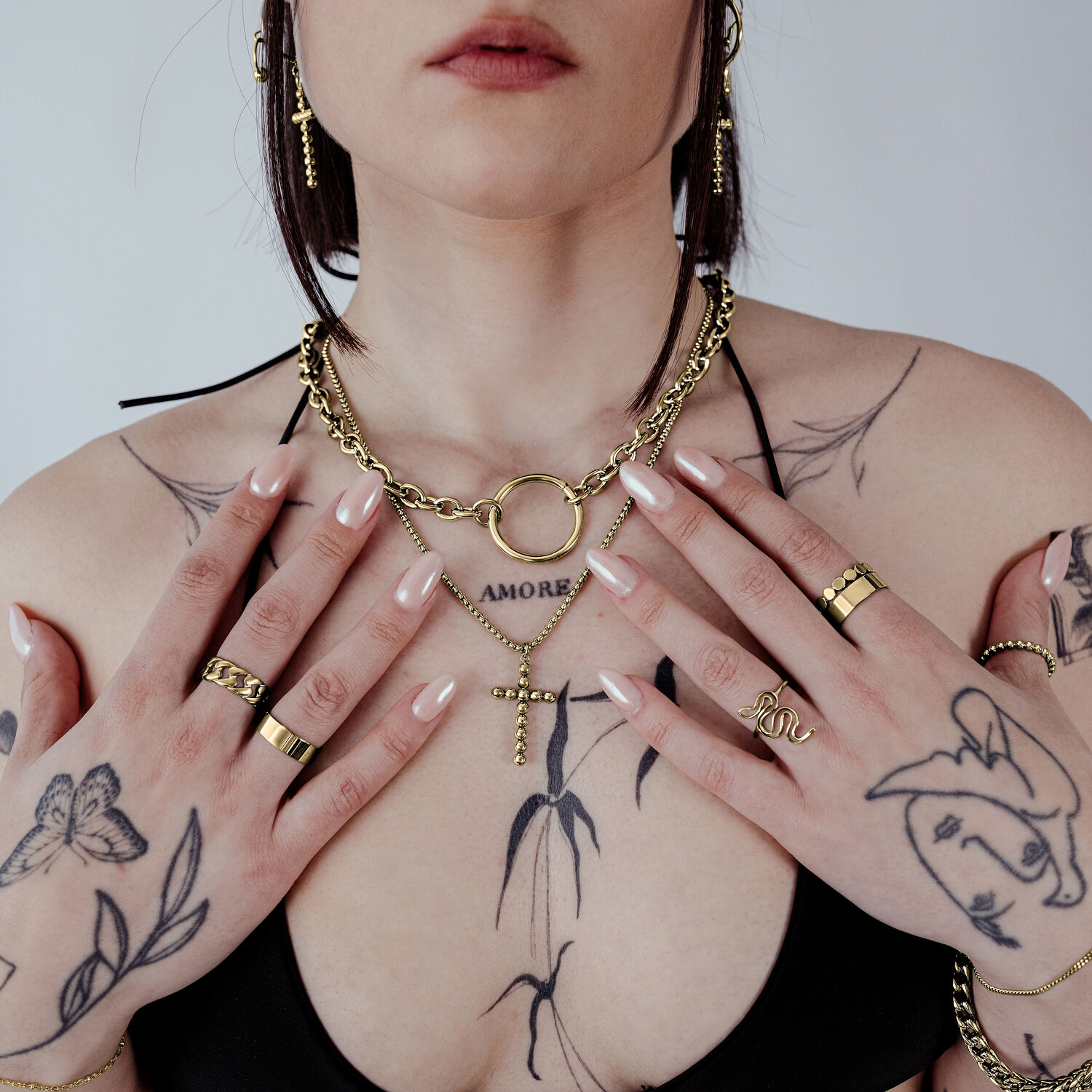 Mujer con collar Cruz de Burbujas dorado y tatuajes sobre fondo claro
