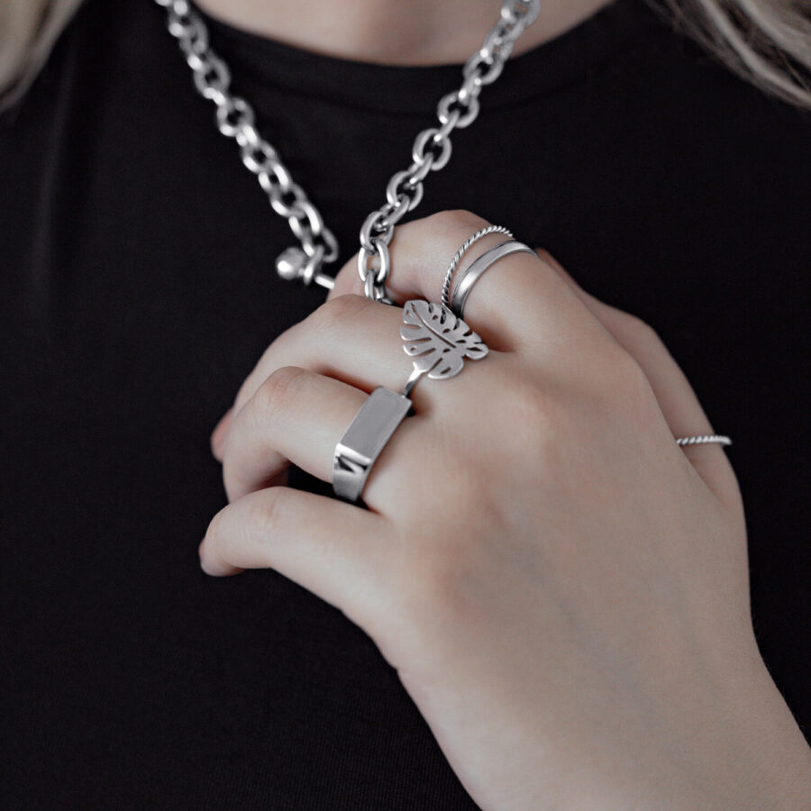 Anillo plateado de hoja de Monstera en la mano, usado con otros anillos