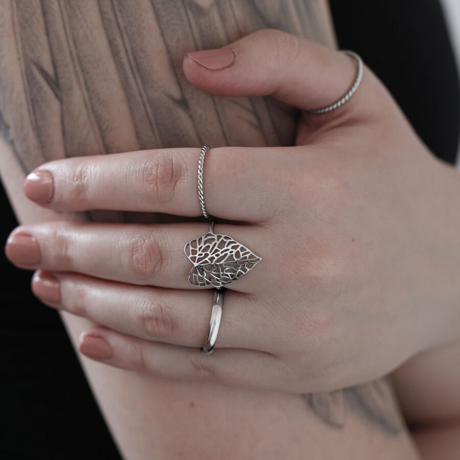 Anillo de hoja plateado de acero quirúrgico en una mano tatuada sobre un fondo claro