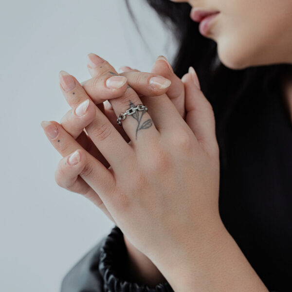 Anillo de eslabones de plata en las manos de una persona con dedos tatuados y mangas negras