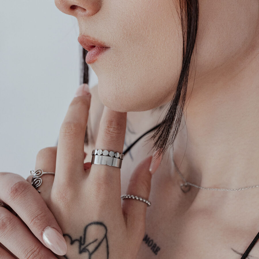 Primer plano de un anillo unisex de placas finas en el dedo, plata, piel con tatuajes de fondo