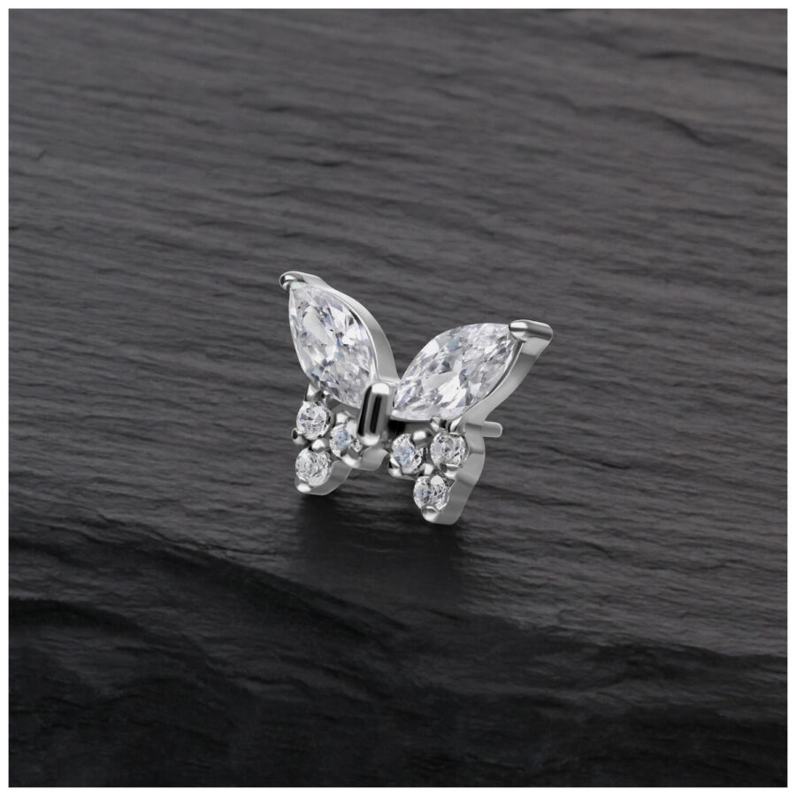 Accesorio de piercing de mariposa plateado con cristales claros sobre fondo oscuro