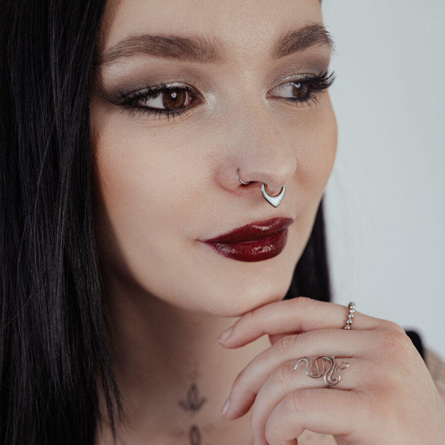 Mujer con cabello negro lleva un septum clicker plateado con opalo sobre fondo claro