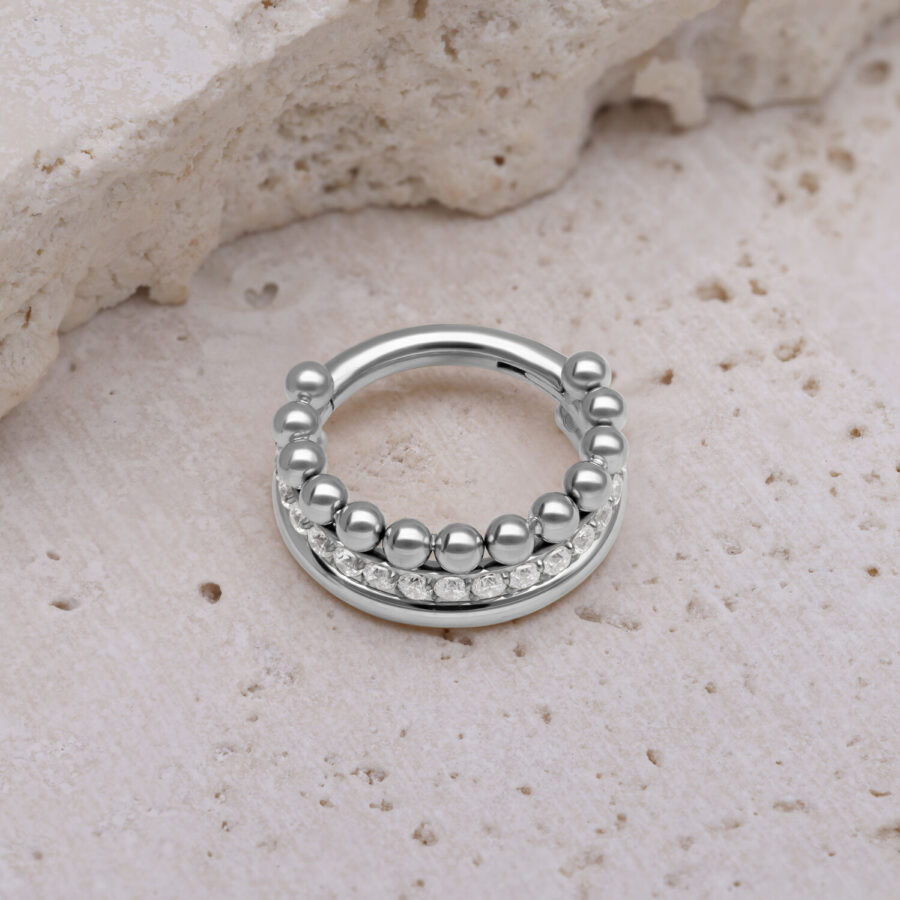 Triple Bubble Clicker plateado con cristales blancos sobre piedra beige