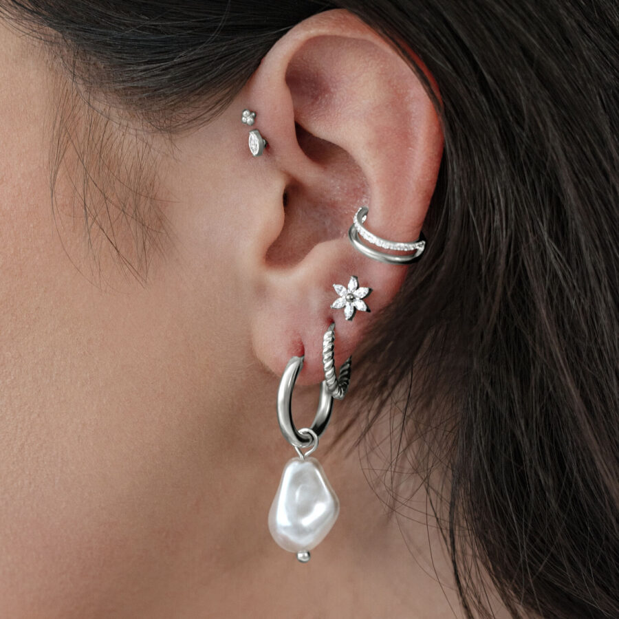 Pendientes de perlas barrocas plateadas en una oreja con varios piercings.