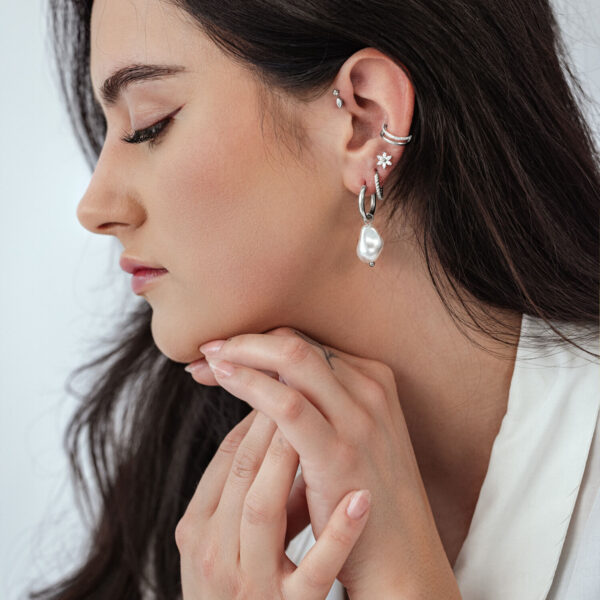 Vista lateral de una mujer con aros de perlas barrocas y otros pendientes sobre fondo claro