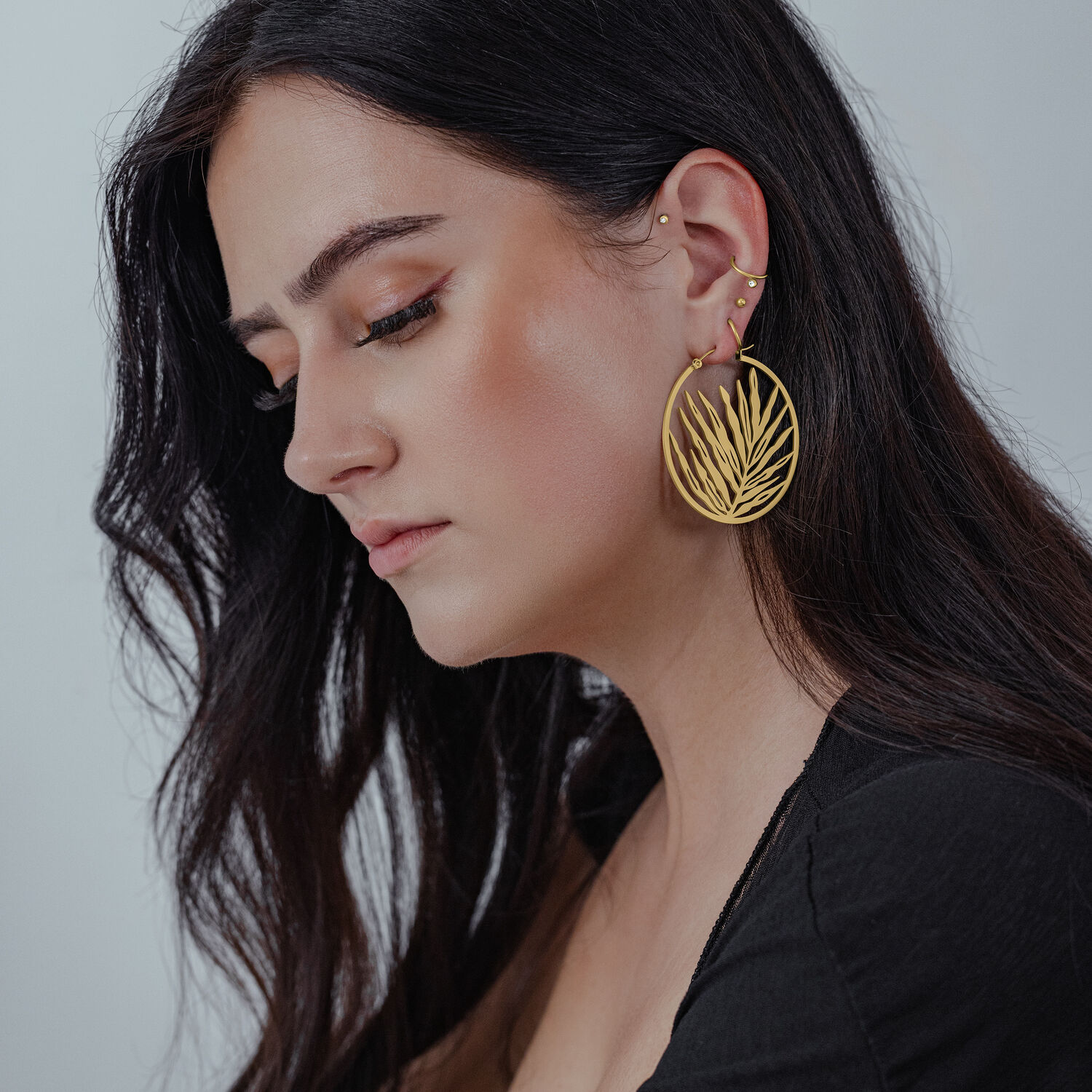 Aros dorados Noble Leaf Mujer lleva aros dorados Noble Leaf frente a un fondo neutro