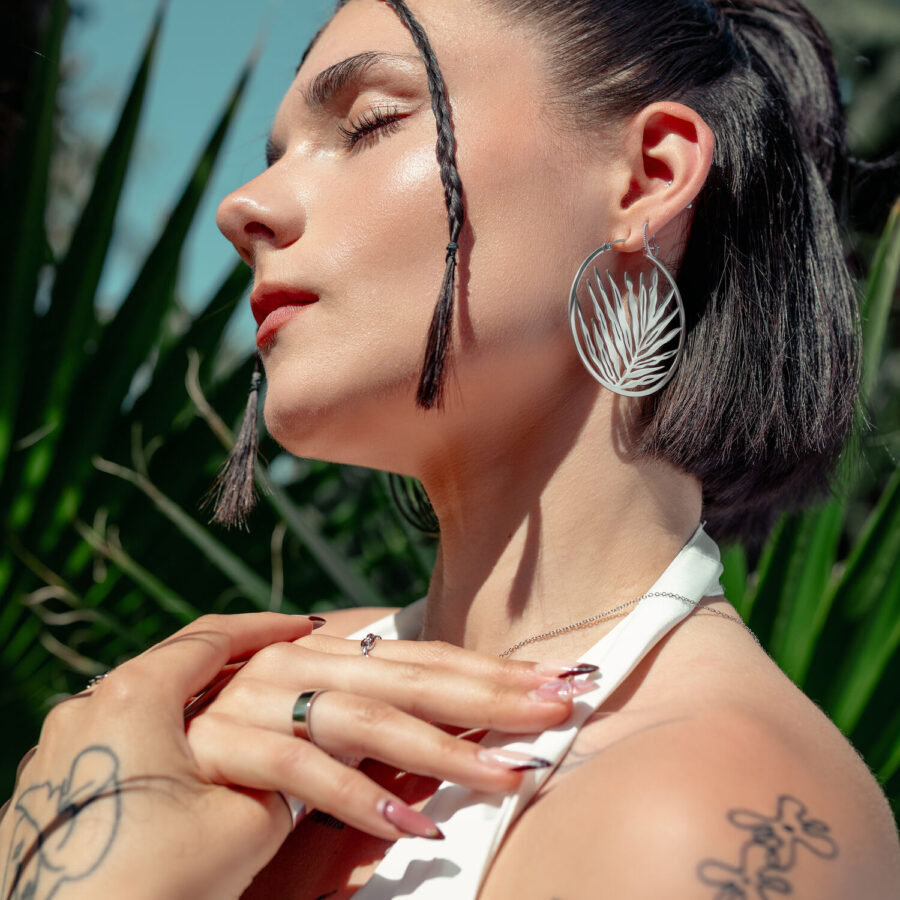 Mujer con grandes pendientes plateados frente a una planta verde