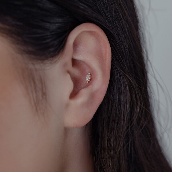 Primer plano de una oreja con colgante en Oro 14K con Moissanita sobre fondo neutro