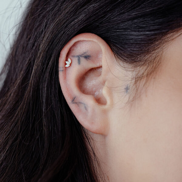Primer plano de un piercing de oreja con Lotus de 14K Gold y ópalo sintético