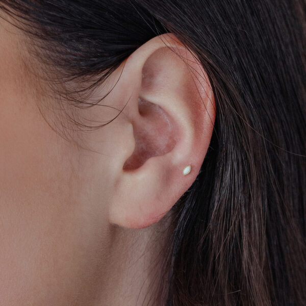 Colgante dorado ovalado con ópalo sintético en la oreja sobre fondo claro