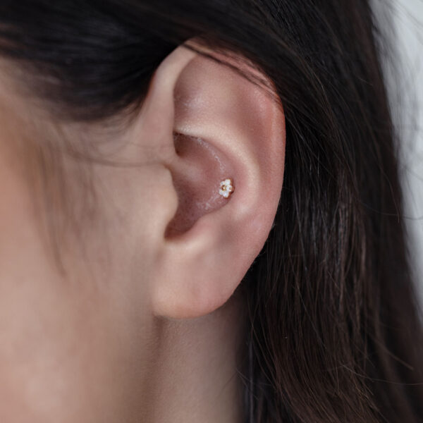 Primer plano de una oreja con un accesorio de flor de oro 14K con ópalo