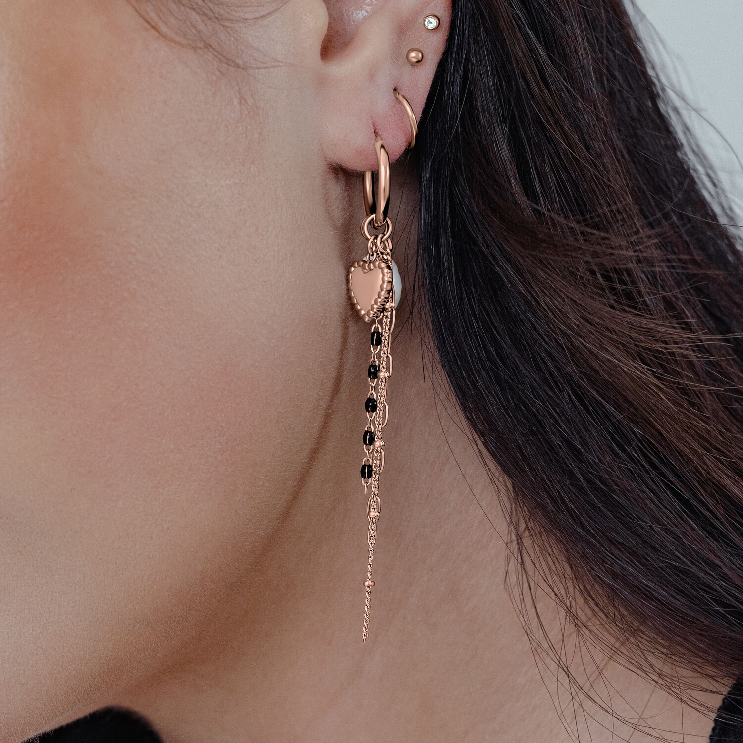 Roségoldene Ohrstecker mit Herz und hängender Kette an einem Ohr getragen