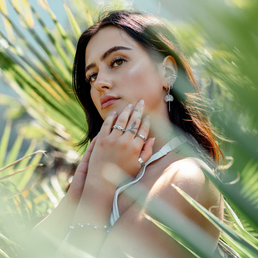Mujer con pendientes Little Petticoat Hoops frente a hojas verdes