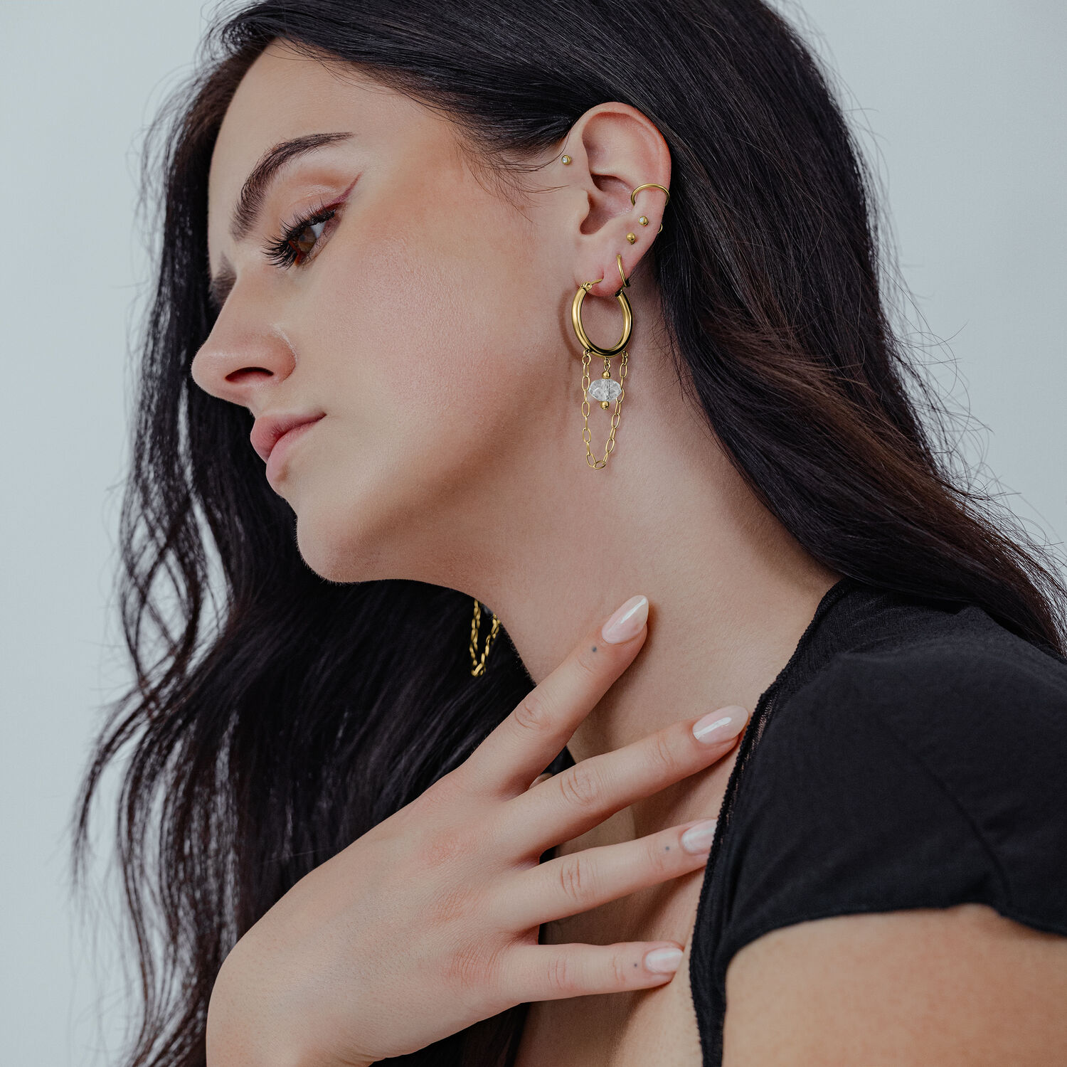 Frau trägt goldene Edgy Stone Hoops Ohrringe mit weißem Stein auf neutralem Hintergrund